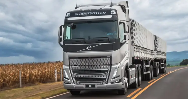Caminhao Volvo FH 540 na cor prata em uma estrada asfaltada com fazendas ao seu redor